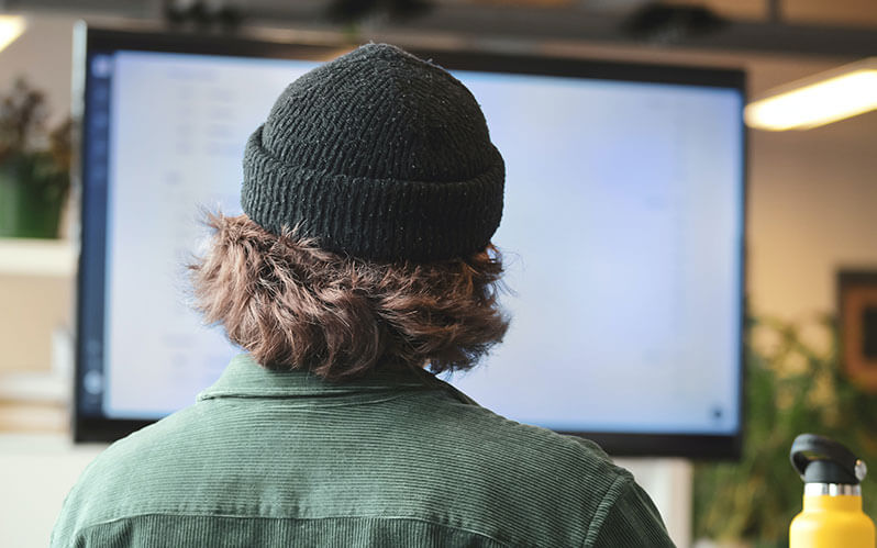 Un homme avec un bonnet en tricot fixe l'écran de son ordinateur.