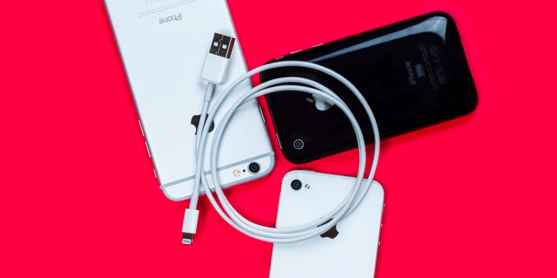 An Apple lightning cable sits on top of three iPhones