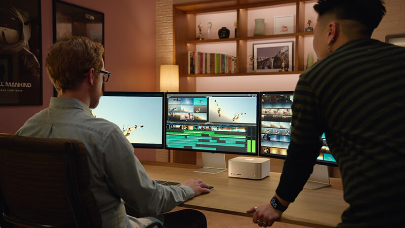 Deux monteurs examinent une ligne de temps sur trois moniteurs reliés à un studio Mac.