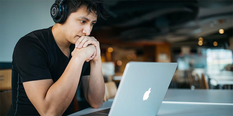 Een man met een koptelefoon op staart aandachtig naar zijn computer  