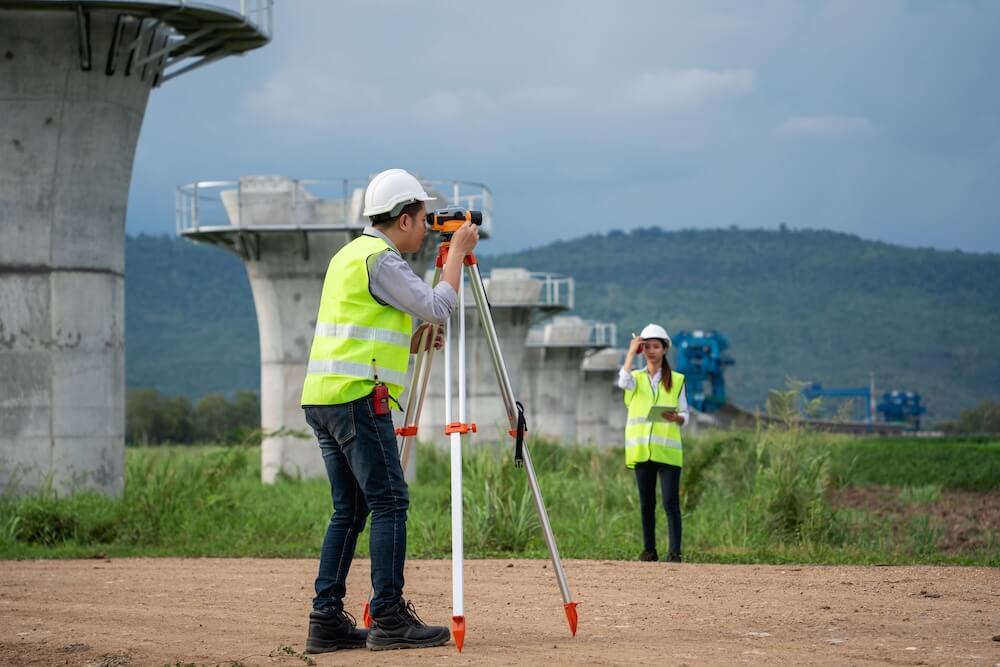 Survey team is working with a theodolite and road construction plans. Civil engineers are taking measurements with surveying tools during the construction. プレースホルダー画像