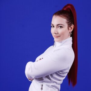 Customer Story: Sarah Barrick's headshot. Confident woman with red hair, arms crossed, against a blue background.