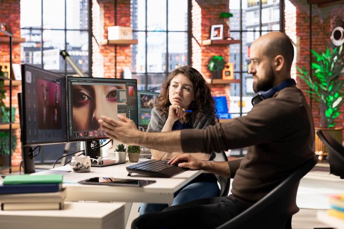 Creative agency team optimizing file transfer workflow, editing images on dual monitors. Collaborative creative process.